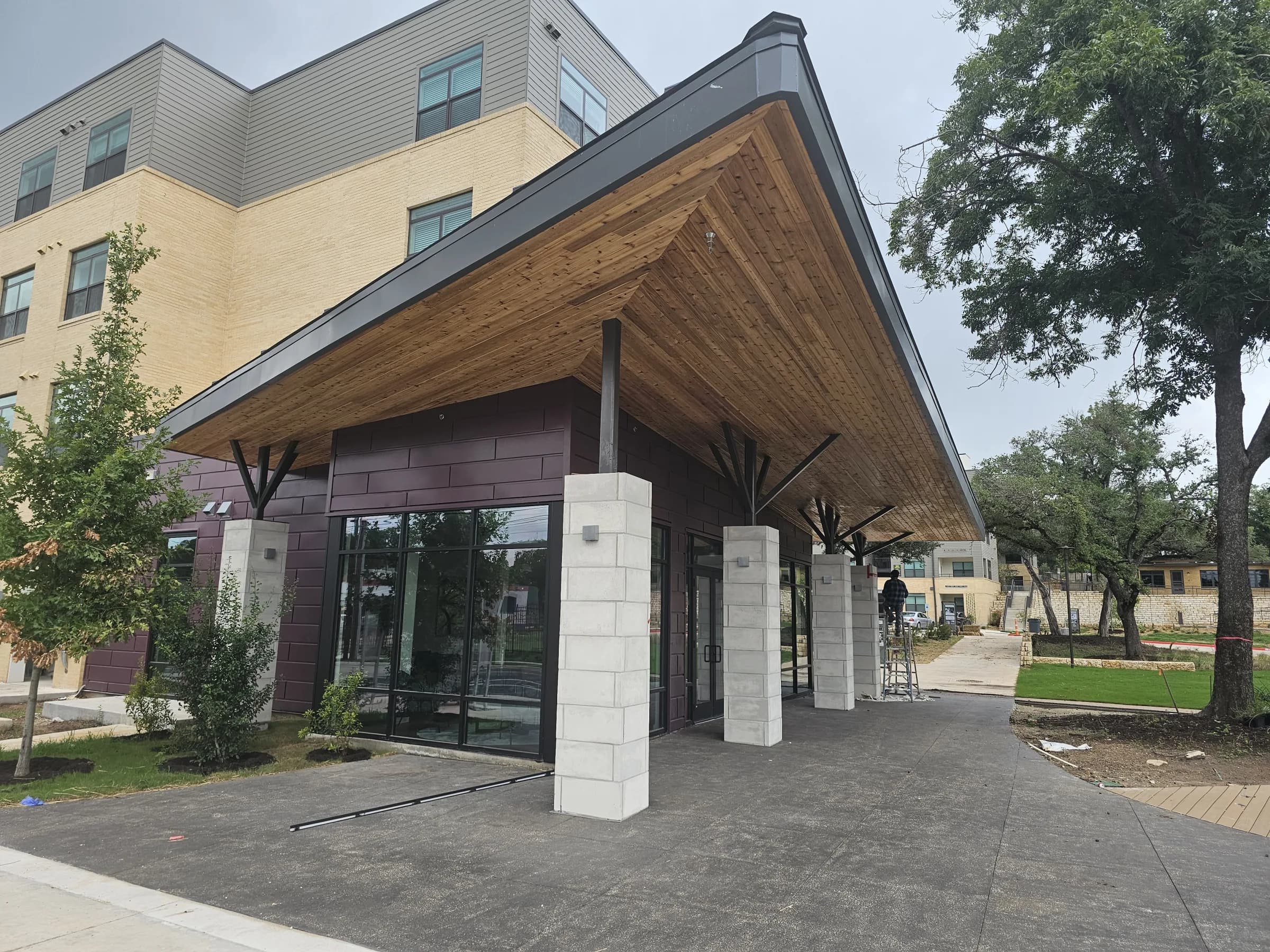 The WOW Heritage Center entrance at Rosewood Courts under construction, cedar canopy overhead, a worker on a ladder finishing the exterior.